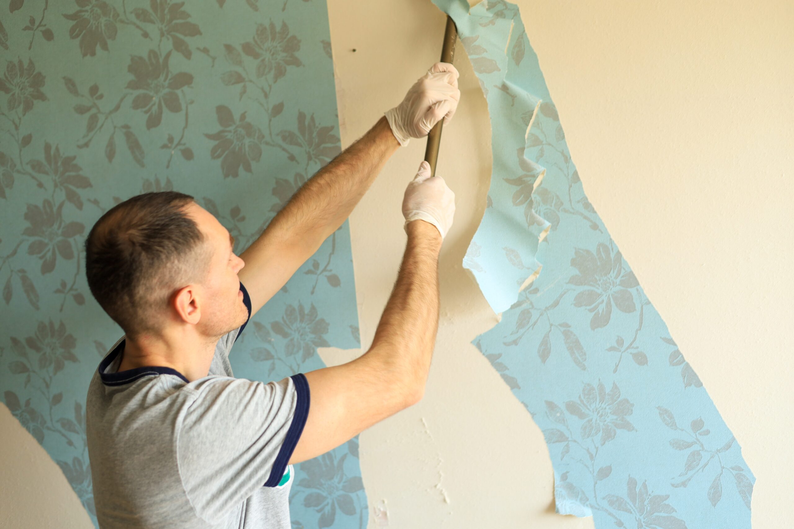 : Contractor removing floral wallpaper from an interior wall while preparing the surface for painting or renovation.