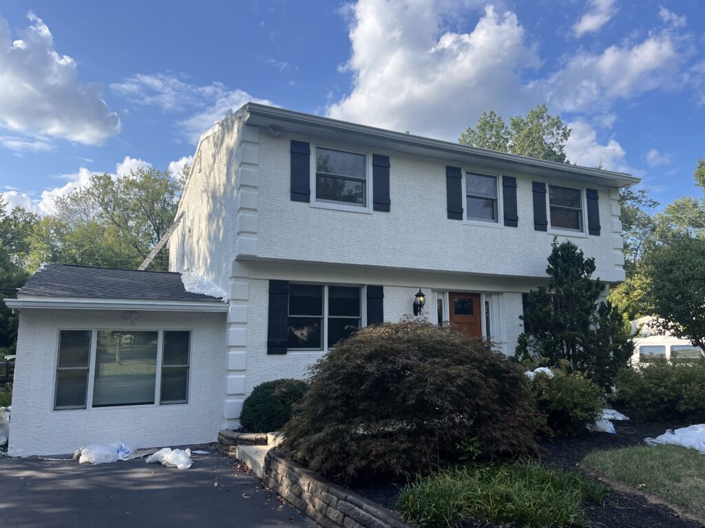 Two-story white stucco home with black shutters, front landscaping, driveway, and blue sky during an exterior home inspection or renovation project
